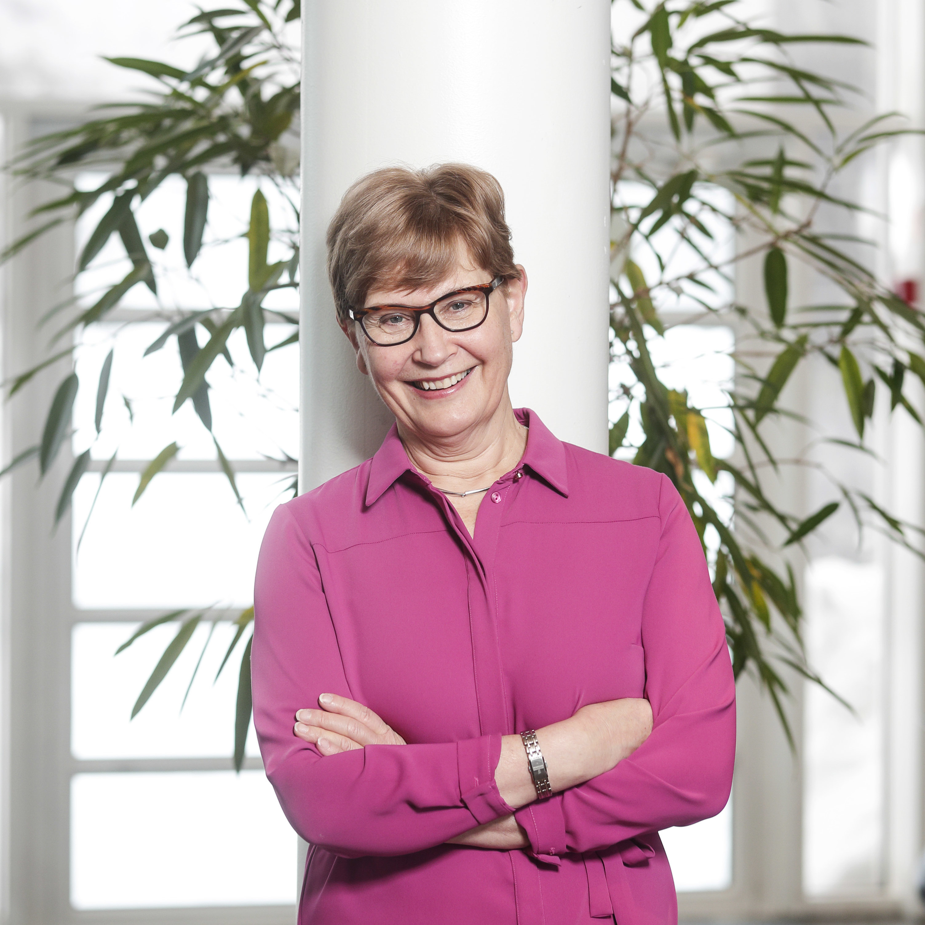 Dr. Anna-Maija Lämsä pozuoja prie lango su augalais fone, vilkinti rožinę palaidinę ir šypsosi. Ji yra projekto bendravadovė iš Jyväskylä universiteto Suomijoje, emerita profesorė.