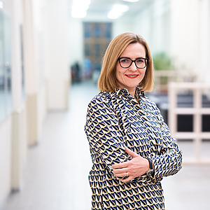 Dr. Raminta Pučėtaitė stovi &scaron;viesiame koridoriuje, vilkinti ra&scaron;tuotą suknelę ir besi&scaron;ypsanti, sukryžiavusi rankas. Ji yra PULSE projekto vadovė ir profesorė.