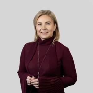 Jolanta Vaičiūnienė stovi &scaron;viesiame fone su sulenktomis priekyje rankomis, vilkinti raudonai violetinę palaidinę plisuotomis rankovėmis. Ji yra projekto darbuotoja, Savivaldos mokymo centro vadovė.
