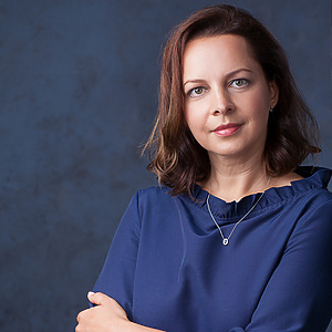 Jūratė Budrienė pozuoja prie&scaron; mėlyną foną, vilkėdama mėlyną palaidinę ir segėdama pakabuką. Ji yra PULSE projekto jaunesnioji mokslo darbuotoja, doktorantė.