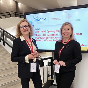 Raminta Pučėtaitė ir Jolanta Vaičiūnienė prie IRSPM konferencijos švieslentės